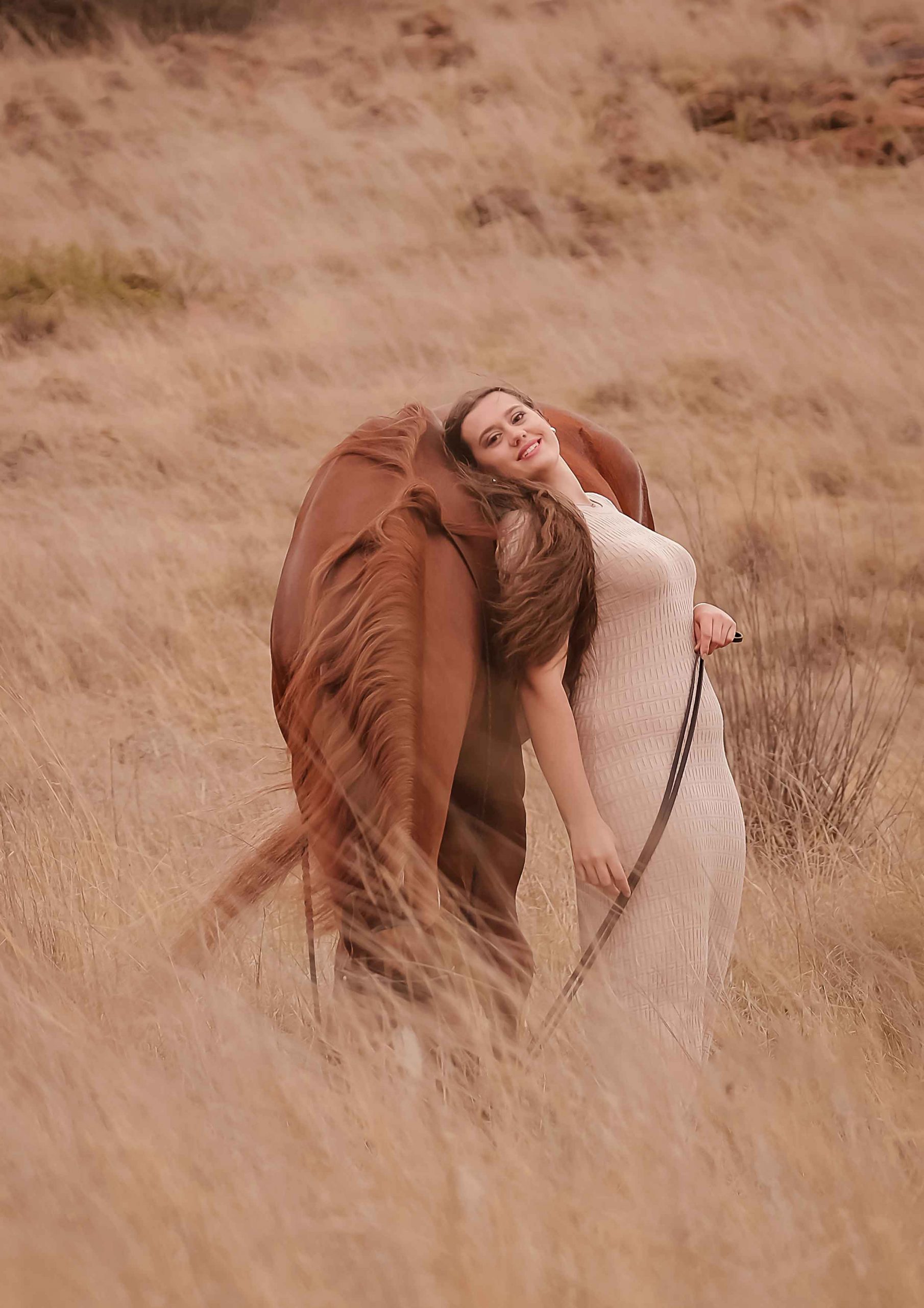 Teenage girl leaning against a chestnut horse's mane in a golden, windswept grass field