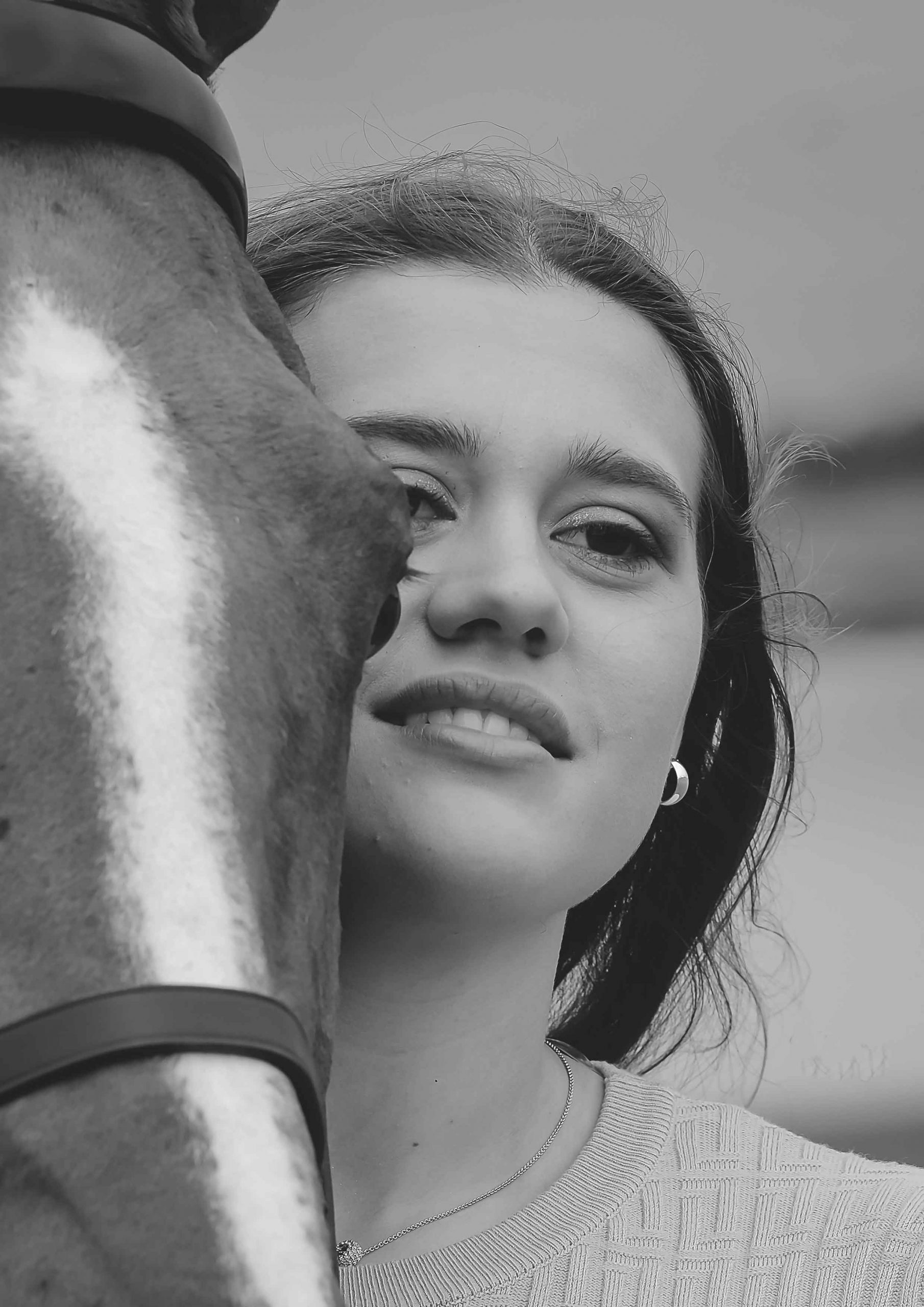 Black and white close-up of a young woman's face resting near a horse's neck and shoulder