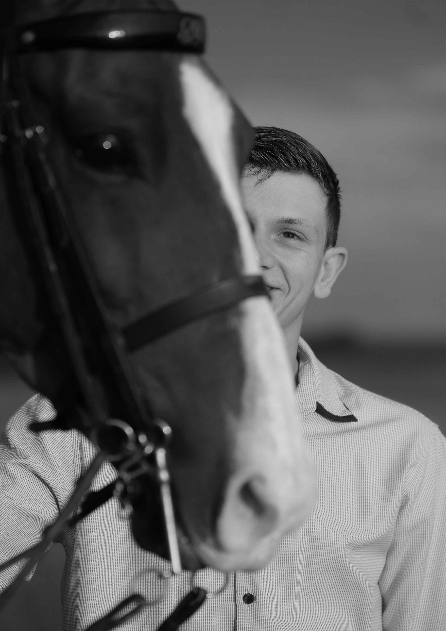Close-up black and white photo of a horse's nose with a teenage boy smiling softly behind it