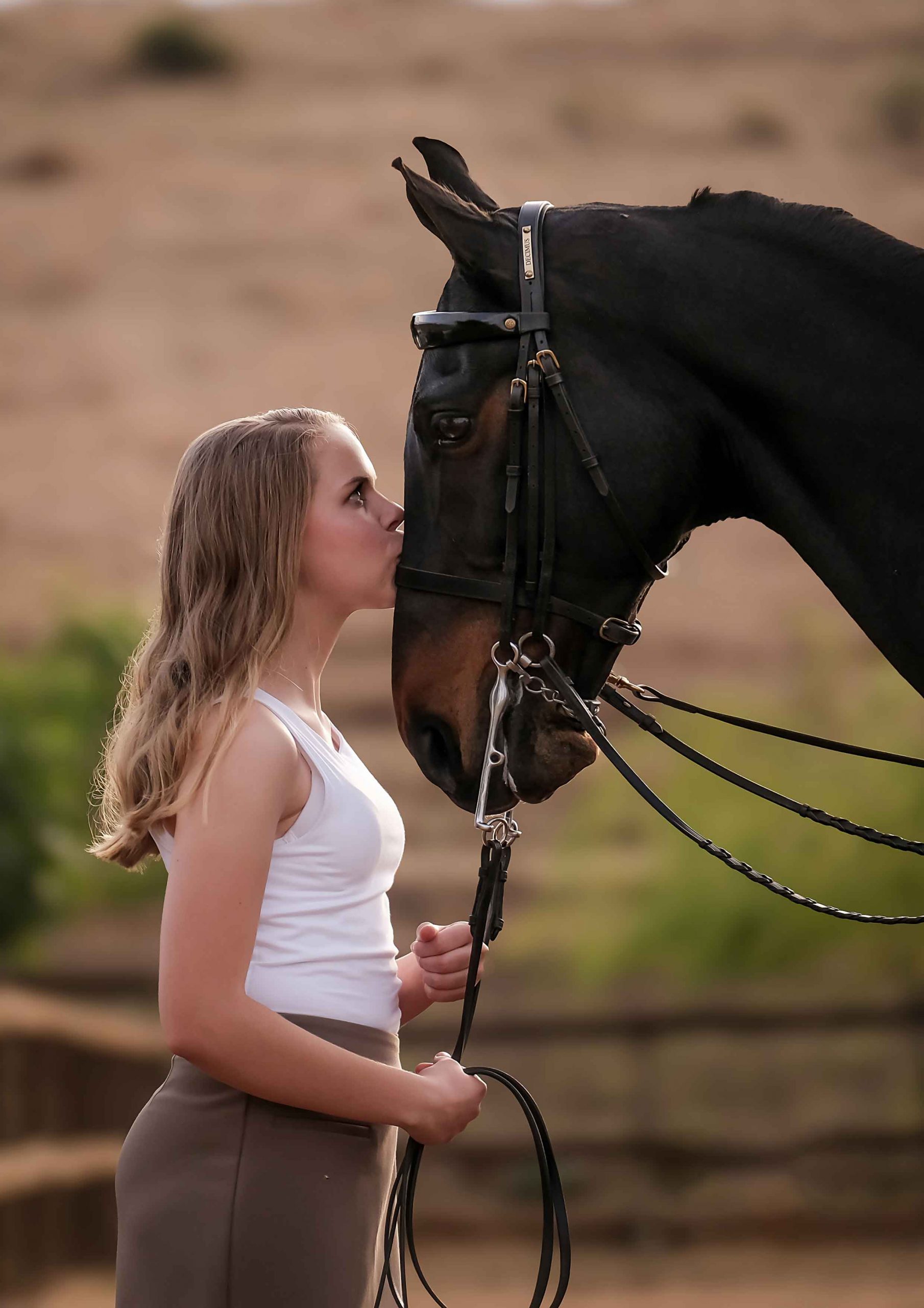Teenage girl in a white top kissing the nose of a dark bay horse wearing a double bridle