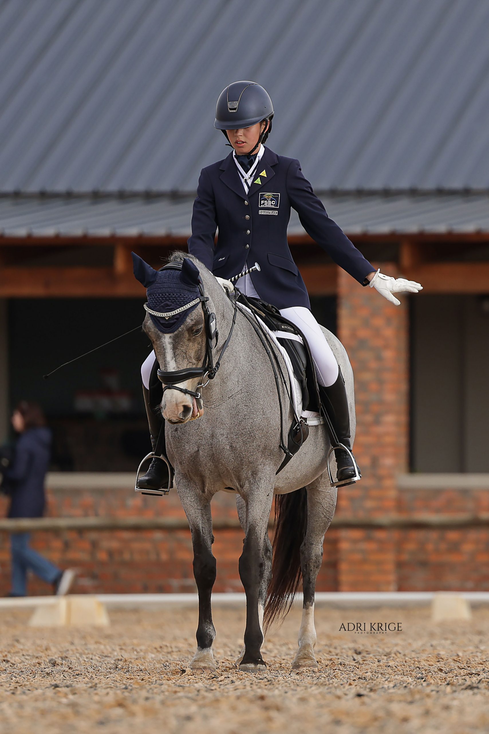 Young dressage rider in a navy jacket and helmet on a grey horse in an arena
