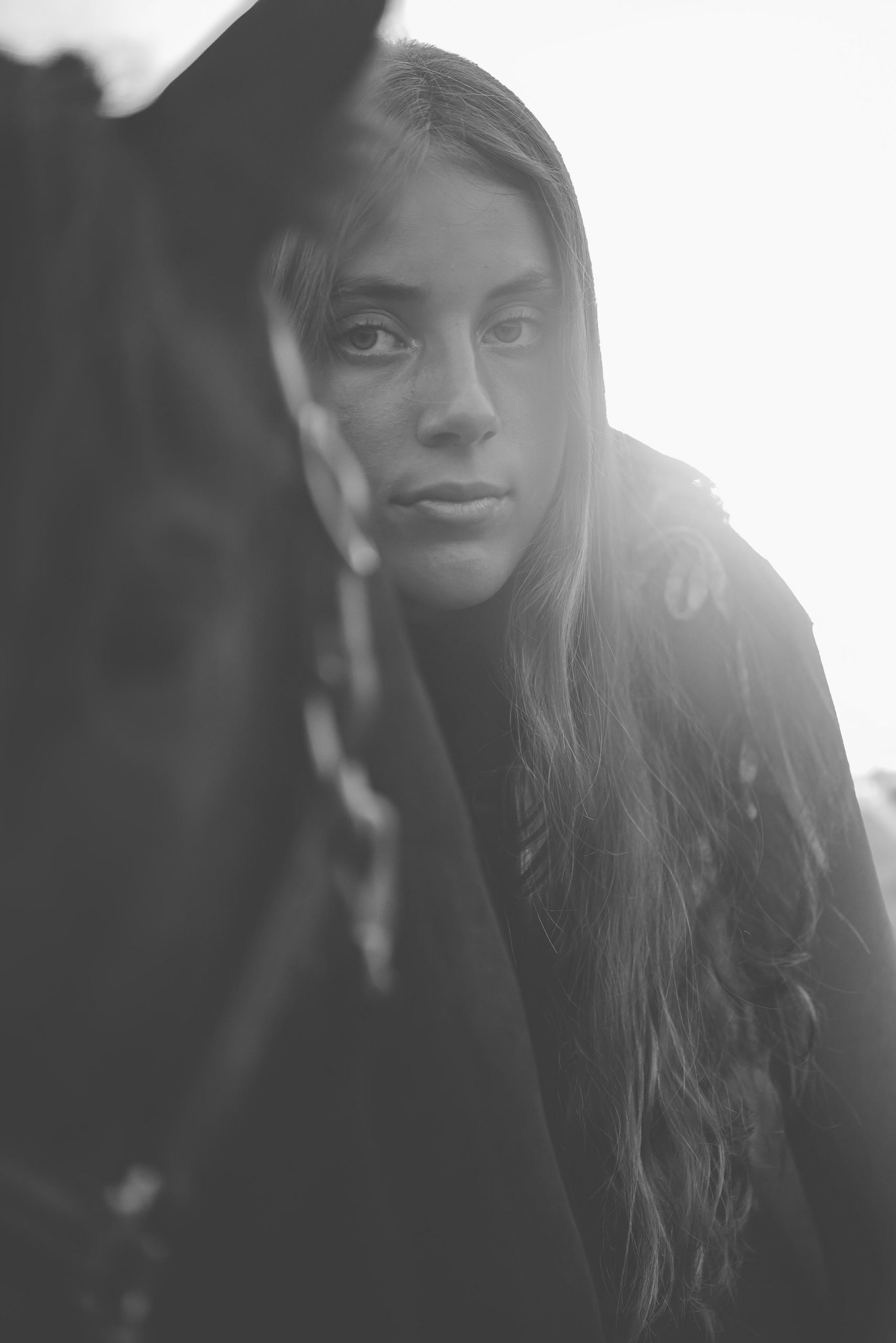 Black and white close-up of a woman's face beside a dark horse's head, softly backlit