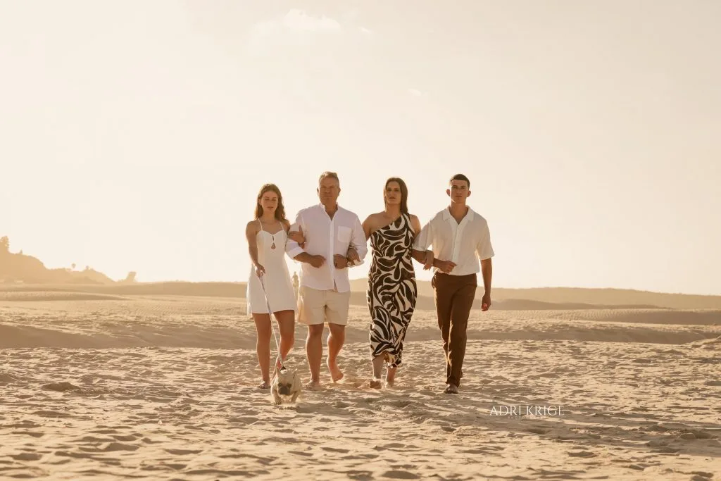 Family of four walking together across the sand on a beach in soft evening light