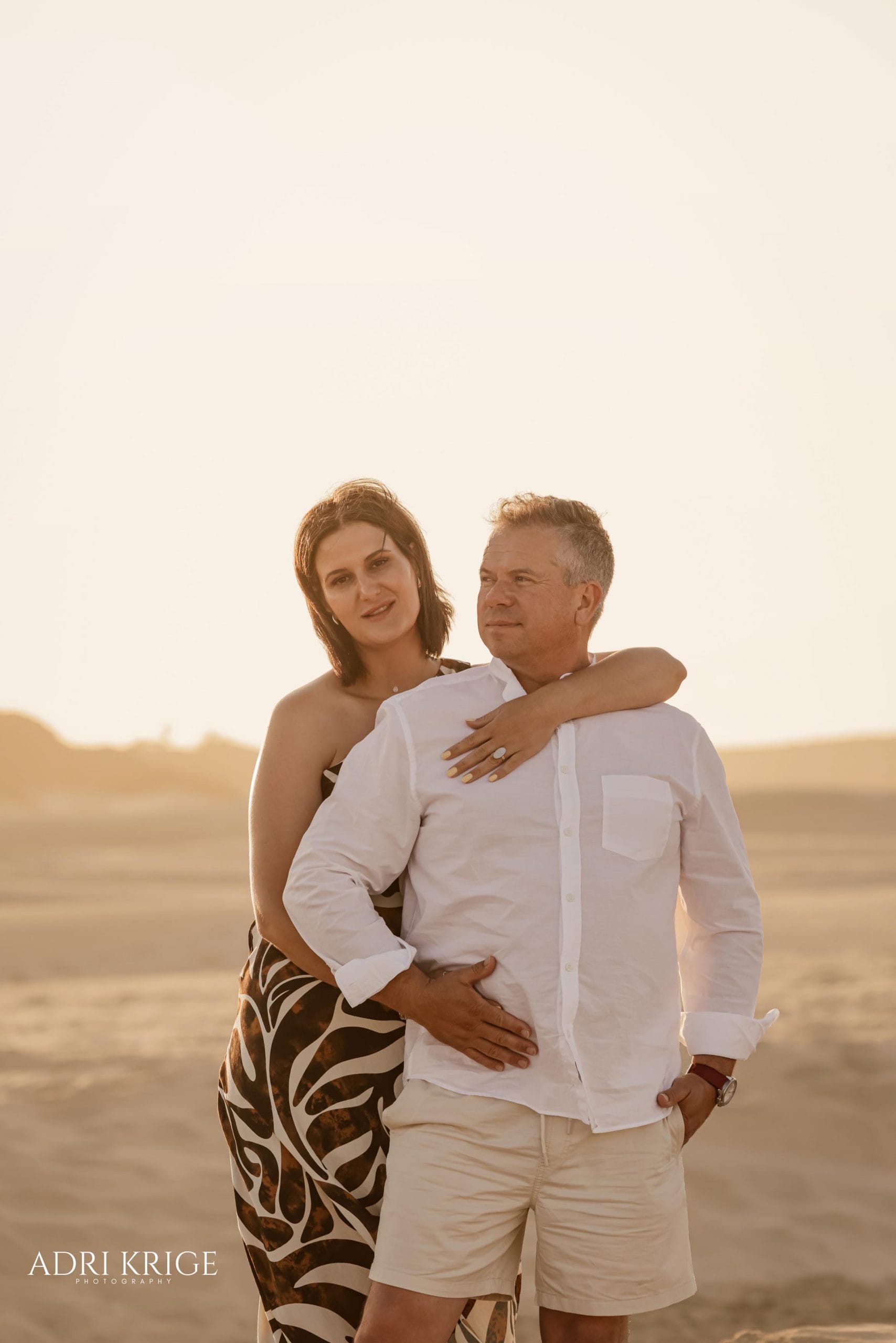 Lifestyle portrait of a mature couple embracing on a sandy beach during sunset.