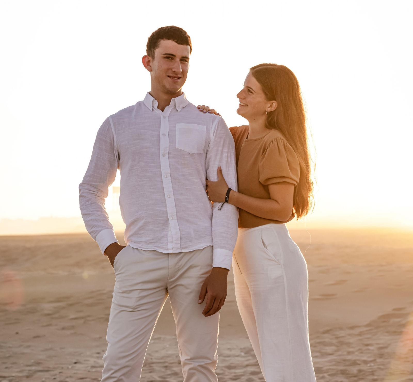 Smiling young couple in white and caramel standing together on the sand at sunset, beach couple photoshoot in Jeffreys Bay by Adri Krige