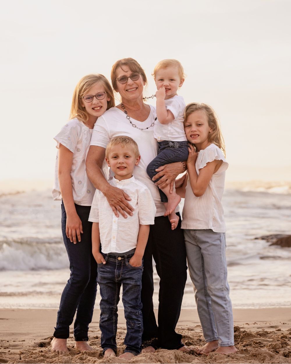 Smiling grandmother on the beach with her four grandchildren in white tops, extended family holiday photoshoot by Adri Krige