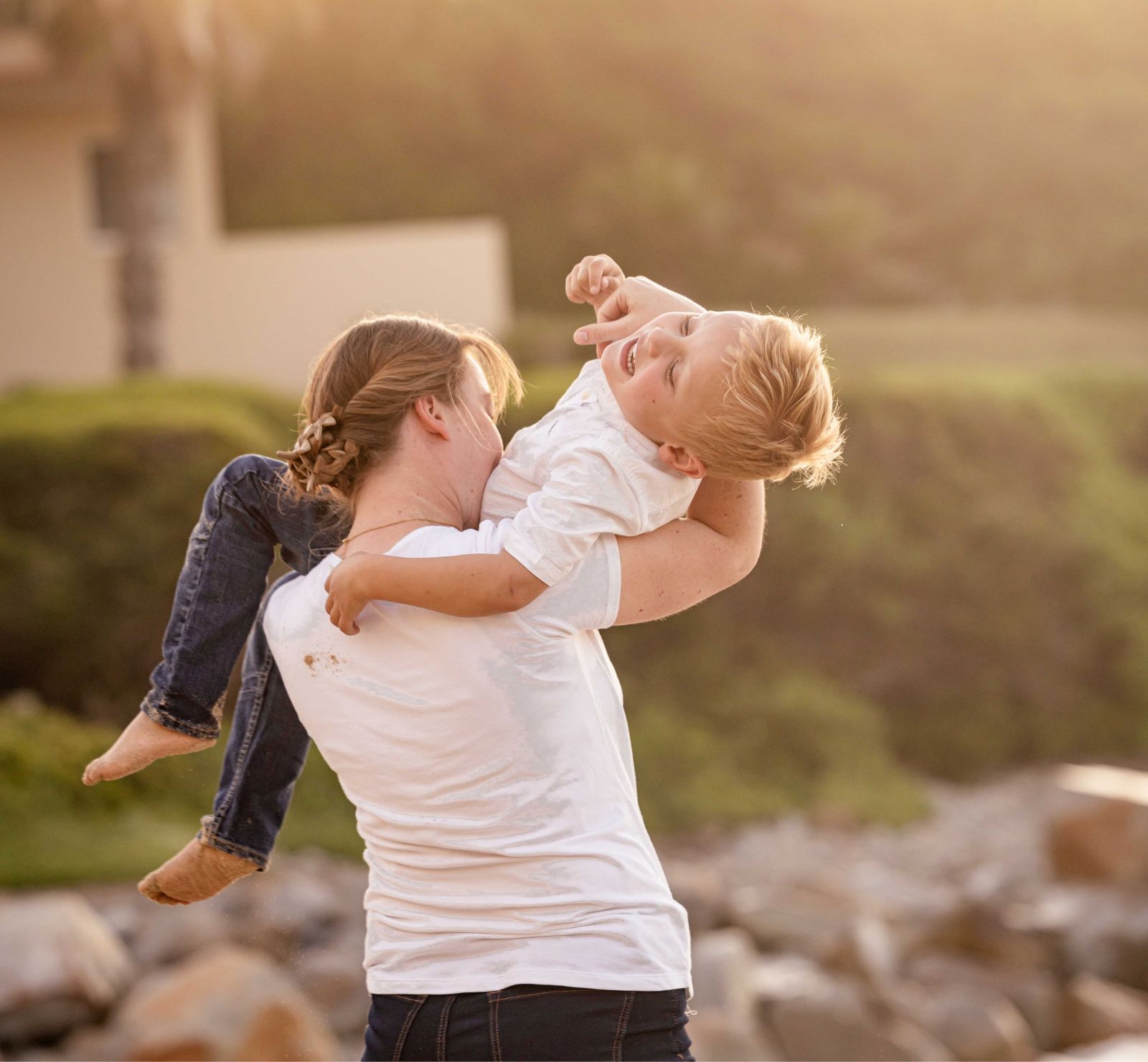 Mother lifting her laughing young son into a hug at golden hour on the coast, family beach photoshoot by Adri Krige