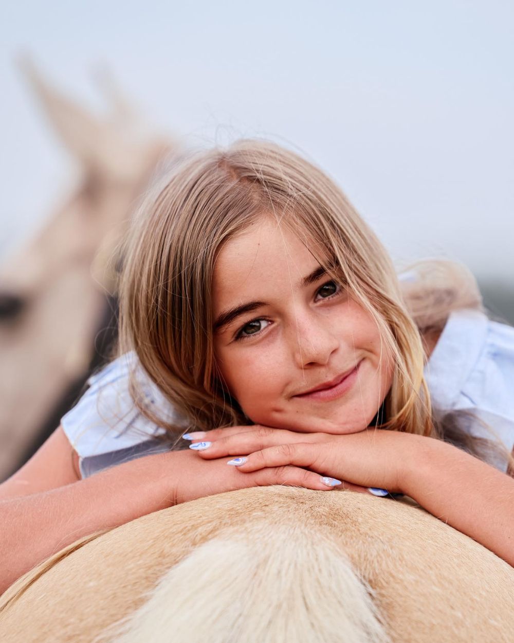 Smiling girl resting her chin on her hands across the back of her palomino horse, horse photography by Adri Krige