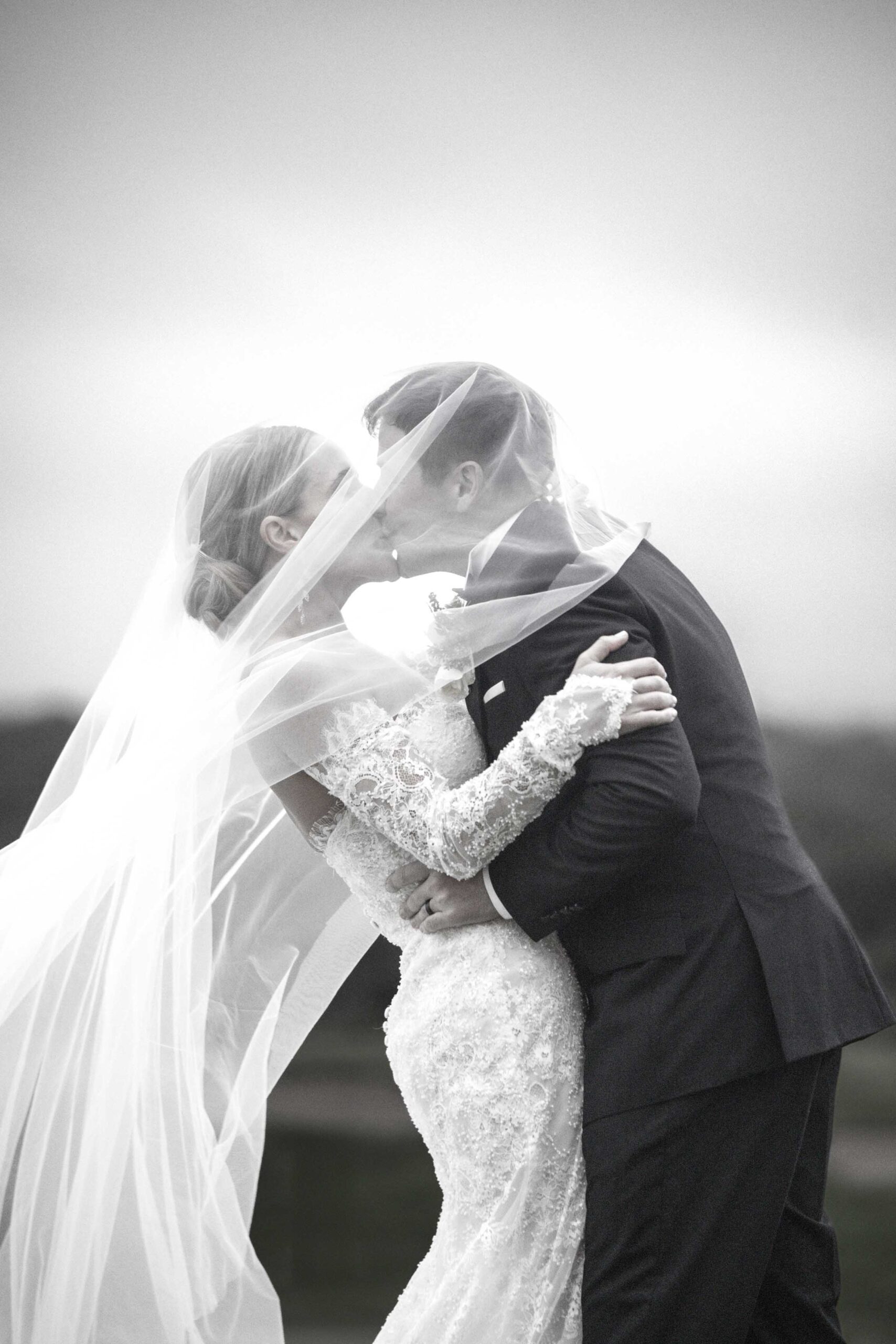 St Francis Links wedding, a kiss beneath the veil Black and white photo of a bride and groom kissing beneath her long veil as it blows in the wind, on their wedding day at St Francis Links, photographed by Adri Krige, wedding photographer St Francis Bay